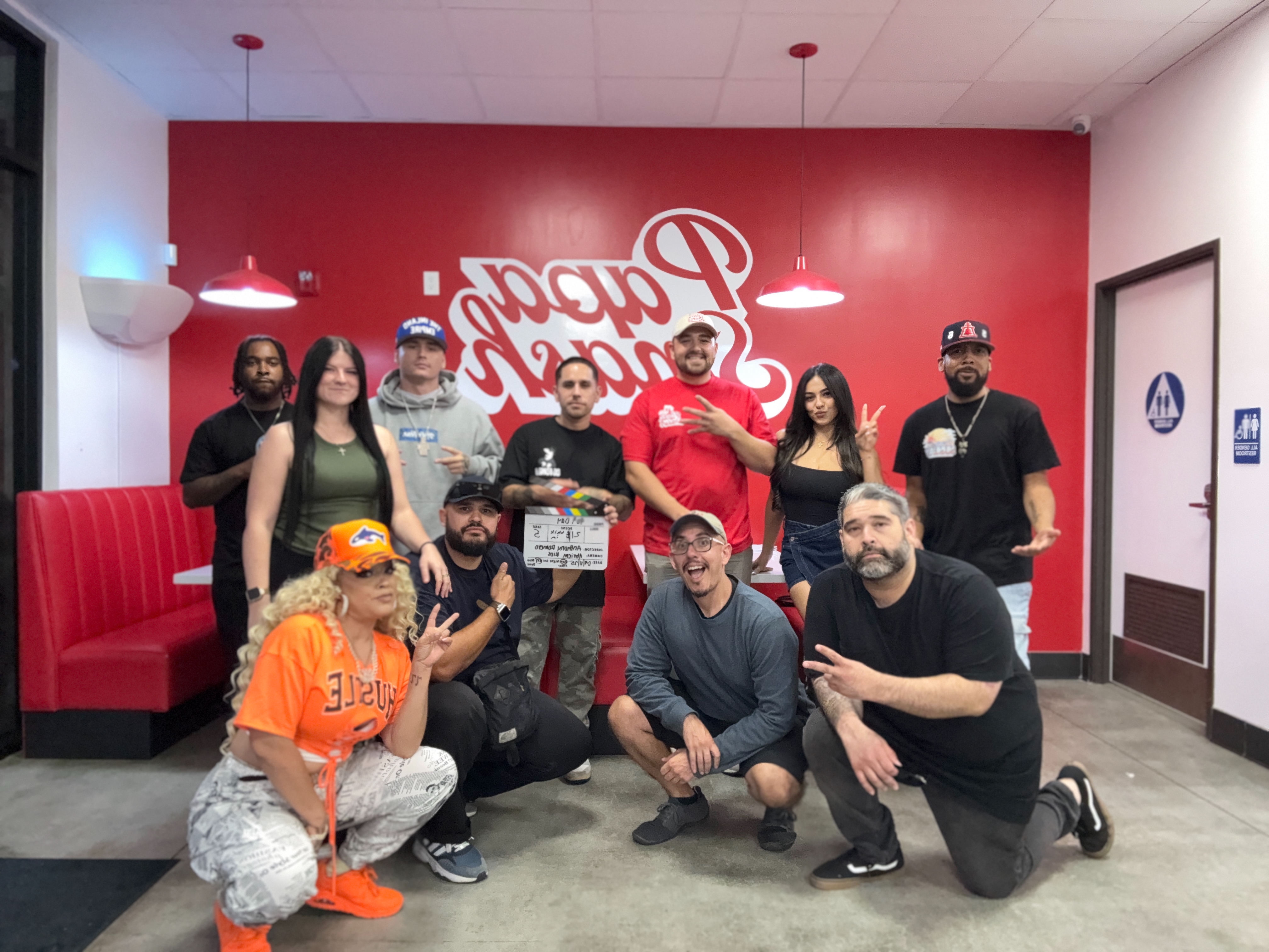 Group photo inside Papa Smash, with a film clapperboard and the restaurant logo on the red wall